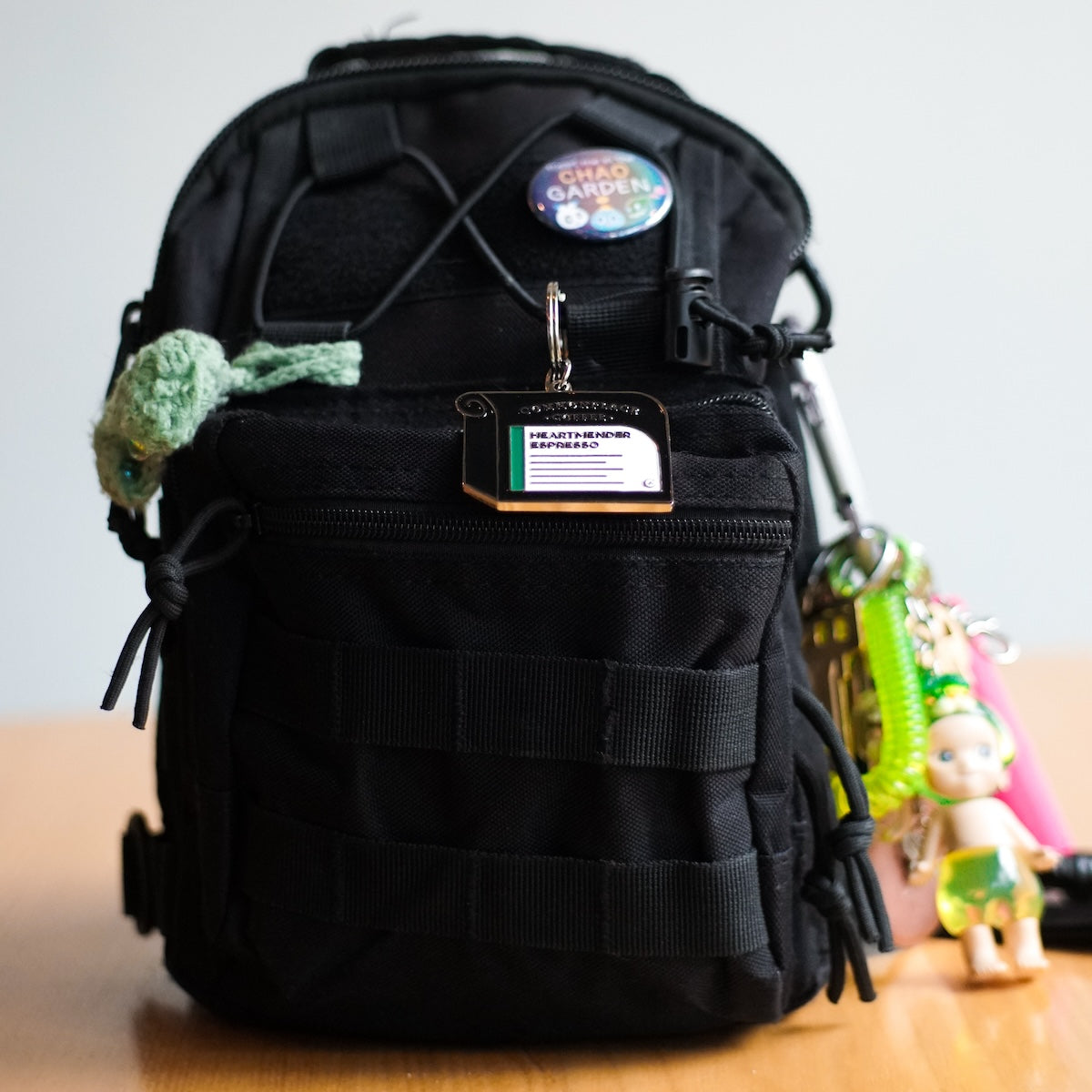 A keychain designed to look like a bag of Commonplace Coffee's Heartmender Espresso hangs on a mini black backpack. 