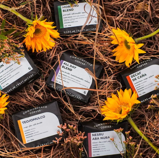 A photo showing bags of Commonplace Coffee beans strewn on top of straw, with sunflowers scattered around them.